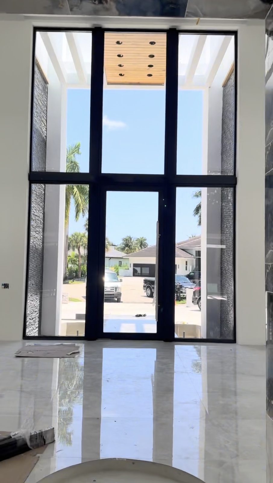 A double-height entrance wall of dark-framed glass with a glazed door at its centre, seen from inside a finished hall with a polished stone floor