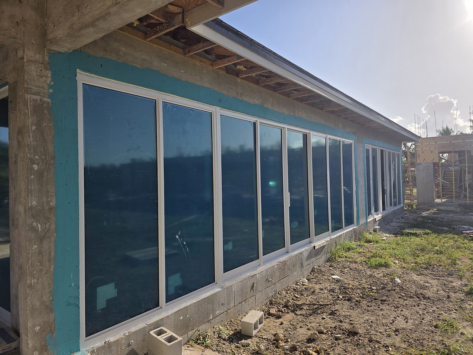 A long run of new white-framed impact glazing receding down the side elevation of a block building, more than a dozen tall bays deep, protective blue film still on every pane