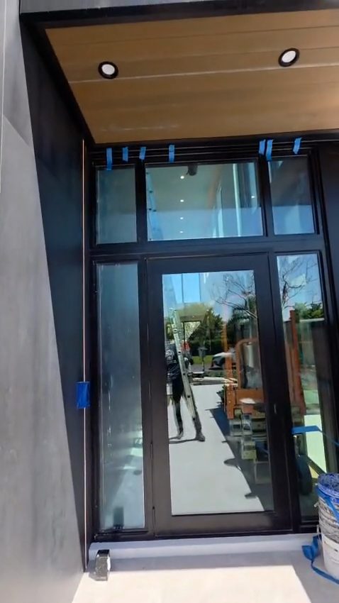 A glazed entrance door with narrow sidelites and a transom above, in dark aluminum, set under a timber-lined soffit